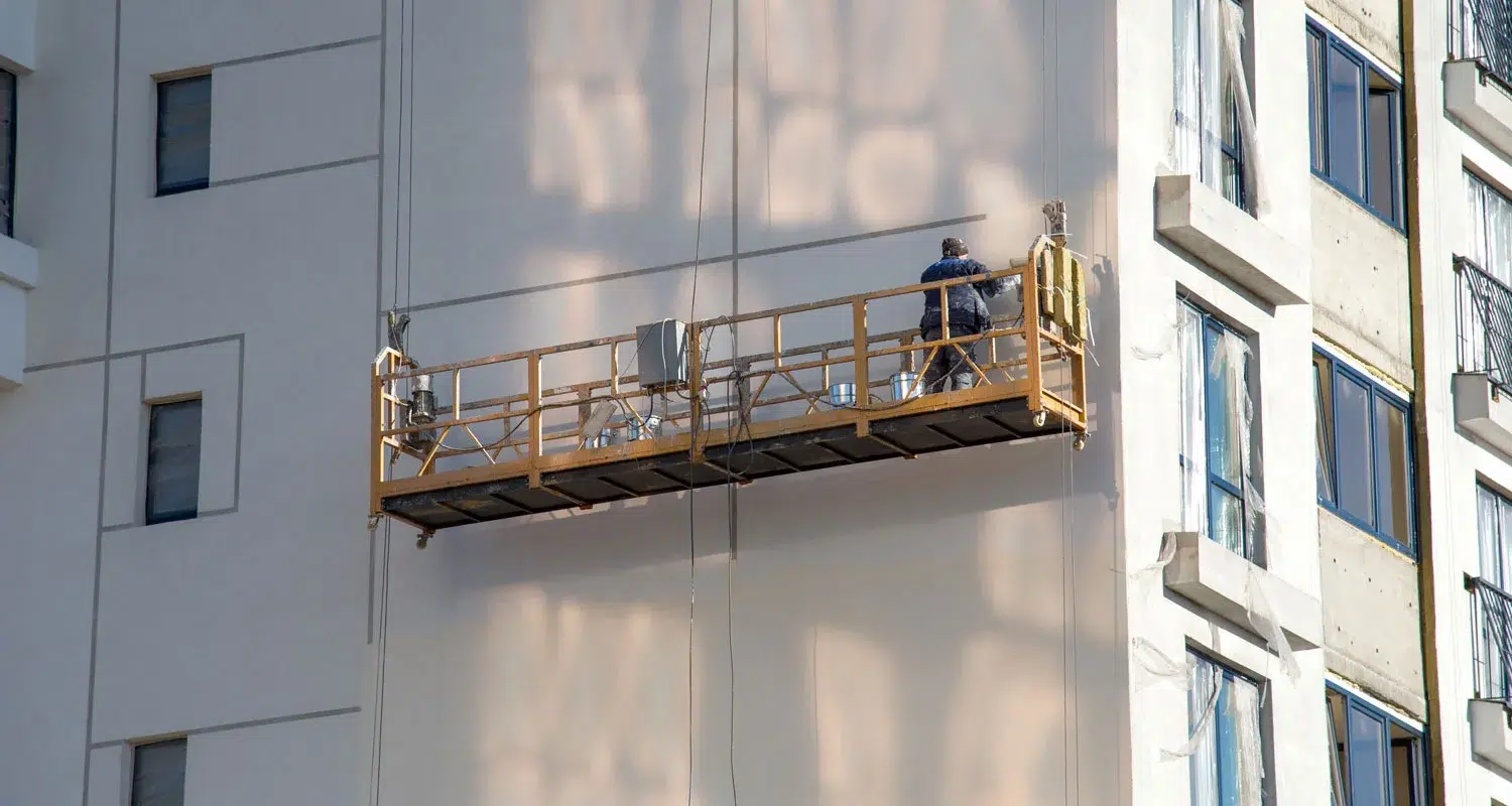 A worker on suspended scaffolding performing maintenance on a high-rise