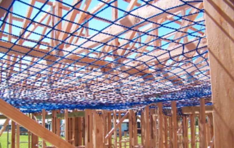 Blue safety netting installed beneath timber roof trusses on a residential build
